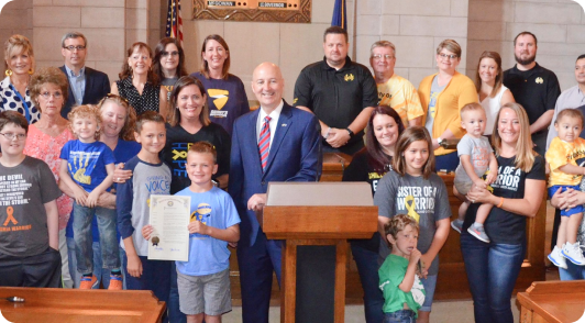 A group of supporters and childhood cancer warriors standing together with a signed proclamation to raise awareness for research funding.